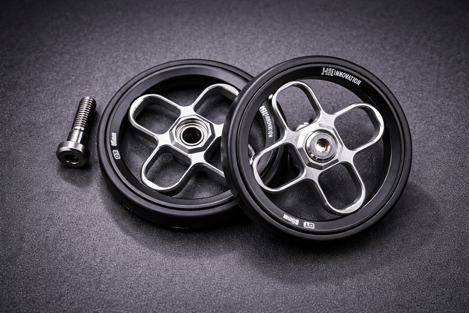 Two metal scooter wheels with black rubber tires and exposed silver spokes are placed on a dark surface, with a metal bolt lying next to them. The wheels are labeled Heli Innovation.