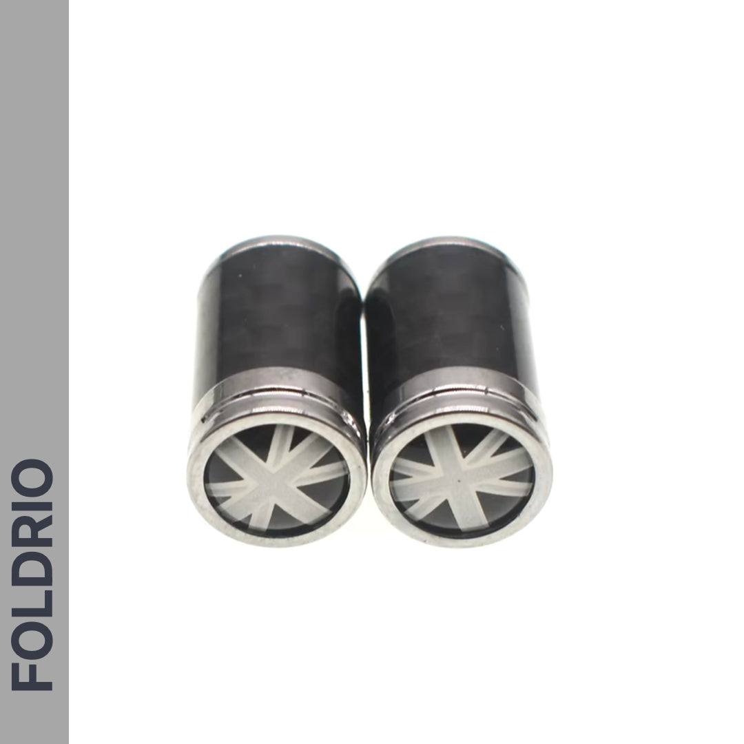 Two cylindrical metallic Brompton Union Jack Valve Caps – Schrader (A/C/G Line) by FOLDRIO, featuring star-shaped end patterns, are placed side by side on a white background with "FOLDRIO" vertically on the left.