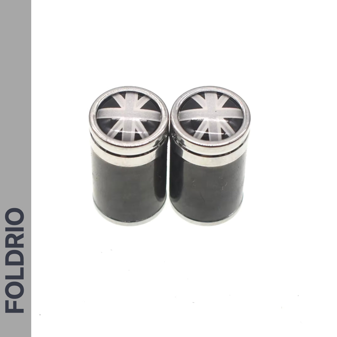 Two black cylindrical containers with metallic lids featuring a monochrome Union Jack are shown side by side. Ideal for storing Brompton Union Jack Valve Caps – Schrader (A/C/G Line) by FOLDRIO, whose name appears vertically on the left.