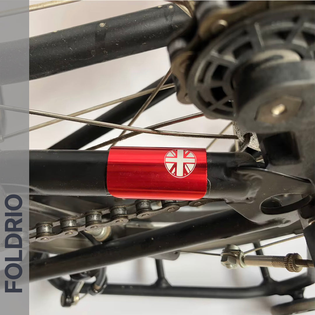 Close-up of a bicycle’s rear wheel, chain, and frame featuring the FOLDRIO Brompton Frame Protector Set with British Flag sticker. "FOLDRIO" appears vertically on the left side.