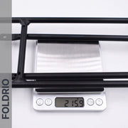 A Brompton Rear Rack – Lightweight Aluminium Cargo Rack, black, is shown on a scale at 215.9g. On the left is a vertical gray banner with “FOLDRIO.” Designed for Brompton easywheel rear rack mounts.