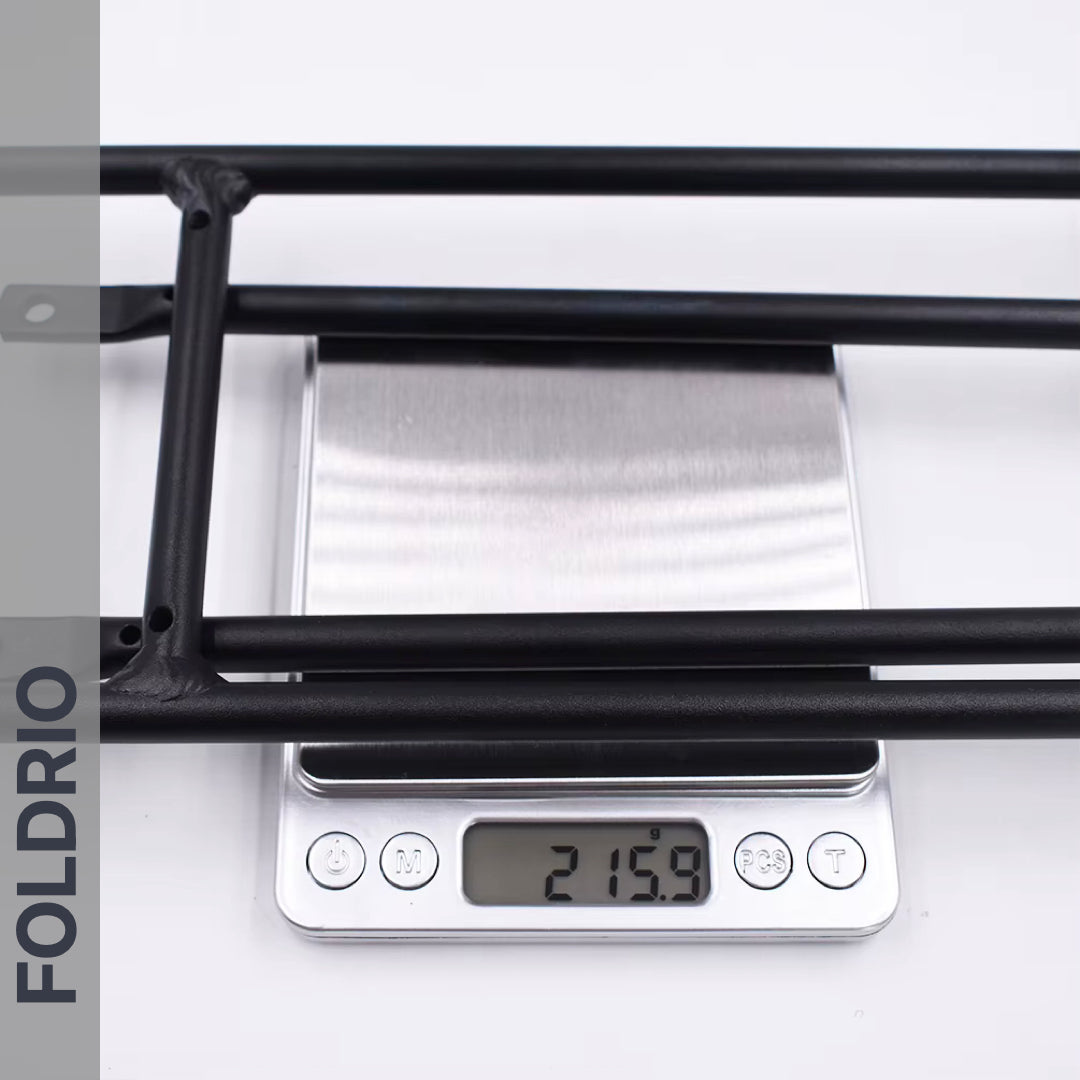 A Brompton Rear Rack – Lightweight Aluminium Cargo Rack, black, is shown on a scale at 215.9g. On the left is a vertical gray banner with “FOLDRIO.” Designed for Brompton easywheel rear rack mounts.