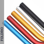 Five anodised aluminium Brompton M Handlebars in blue, red, gold, silver, and black are arranged diagonally on a white background. "FOLDRIO" appears vertically on a gray strip along the left side.