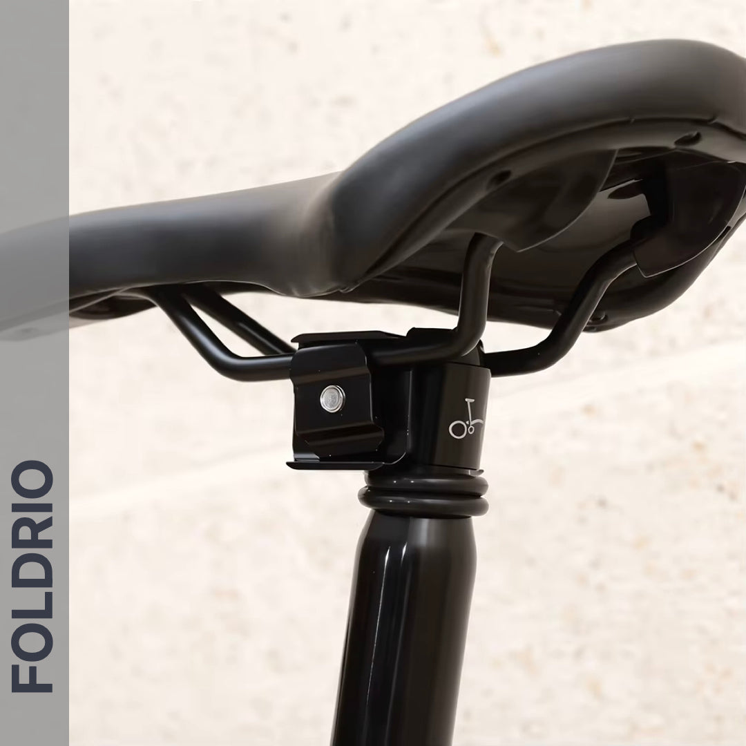 Close-up of a black bicycle seat on a Brompton Titanium Seatpost – Lightweight Upgrade, 560mm & 580mm (31.8mm diameter), with FOLDRIO written vertically on the left side against a gray background.
