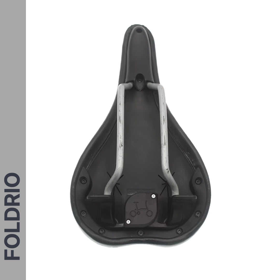 The image shows the underside of a black bicycle seat with metal rails and a mounting area. A Brompton AirTag Saddle Mount – Hidden Tracker Holder is subtly integrated, with FOLDRIO vertically shown on a gray strip along the left side.