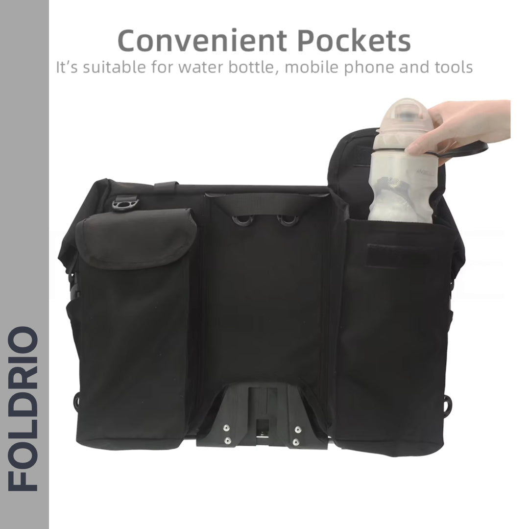The FOLDRIO Brompton Roll-Top Front Bag (27.5L) is shown in black with multiple pockets. A water bottle is placed in a side pocket. Text reads: Convenient pockets for water bottles, mobiles & tools. FOLDRIO branding on the left.