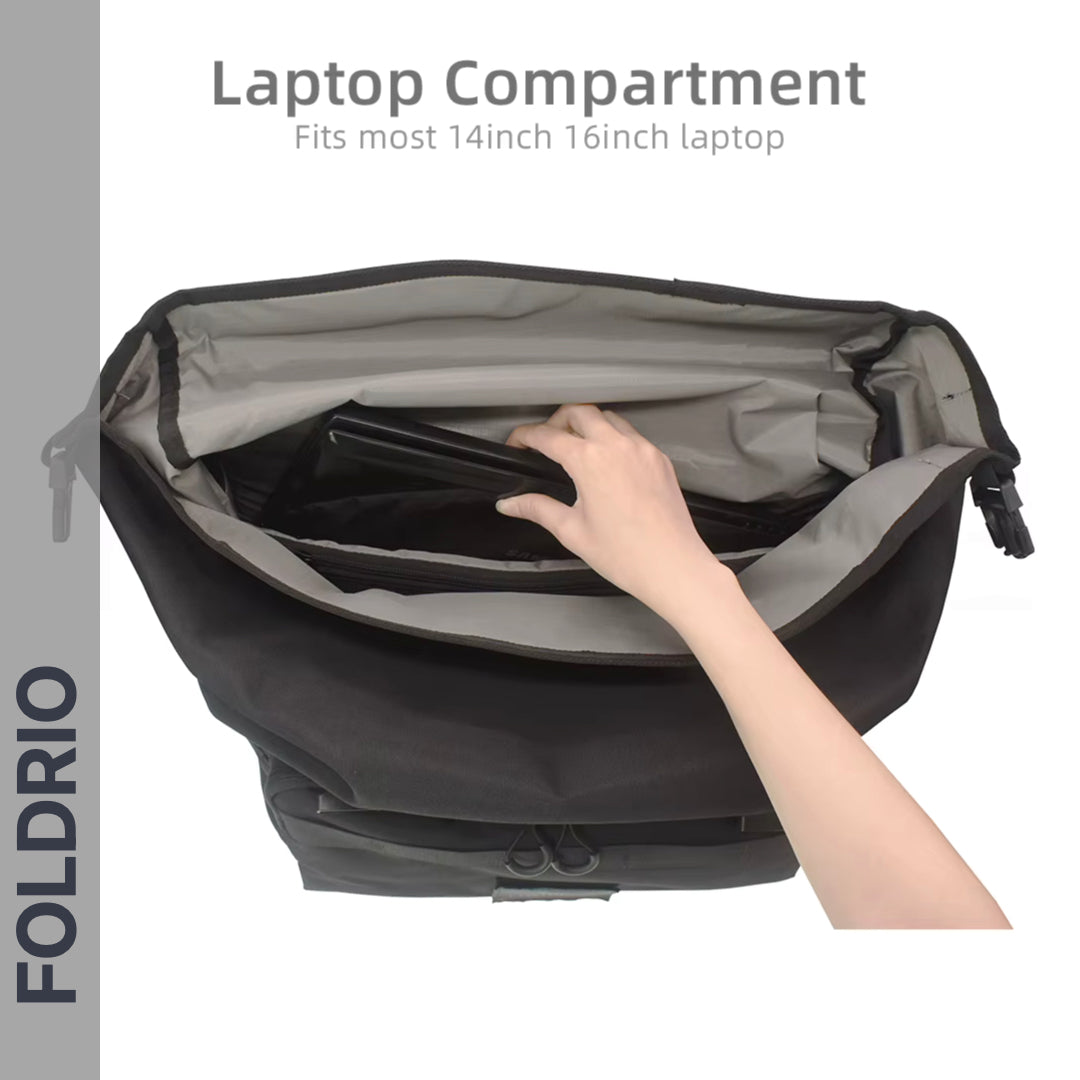 A hand places a laptop into the inner compartment of the black and gray FOLDRIO Brompton Roll-Top Front Bag – 27.5L. Text reads: Laptop Compartment: Fits most 14-inch & 16-inch laptops. 'FOLDRIO' appears vertically on the left.