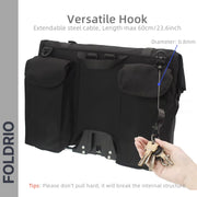 A hand holds keys on a retractable 60cm, 0.8mm steel cable hook from the FOLDRIO Brompton Roll-Top Front Bag (27.5L, Laptop & Commuter). Tip: Avoid pulling too hard on the hook.