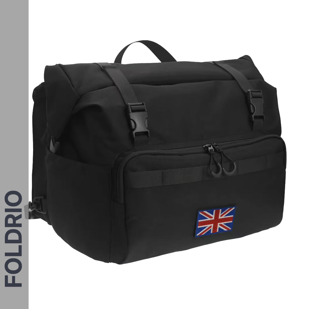 The FOLDRIO Brompton Roll-Top Front Bag (27.5L) is a black commuter backpack with a front zip pocket, two buckle straps, and a UK flag patch. "FOLDRIO" appears vertically on the left side of the image.