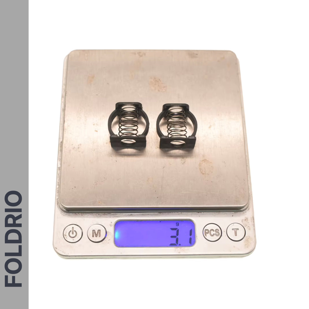Two small black metal Brompton Stem Fixing Buckle Springs from FOLDRIO are shown on a digital scale reading 3.1 grams, with the “FOLDRIO” brand name displayed vertically on the left side of the image.
