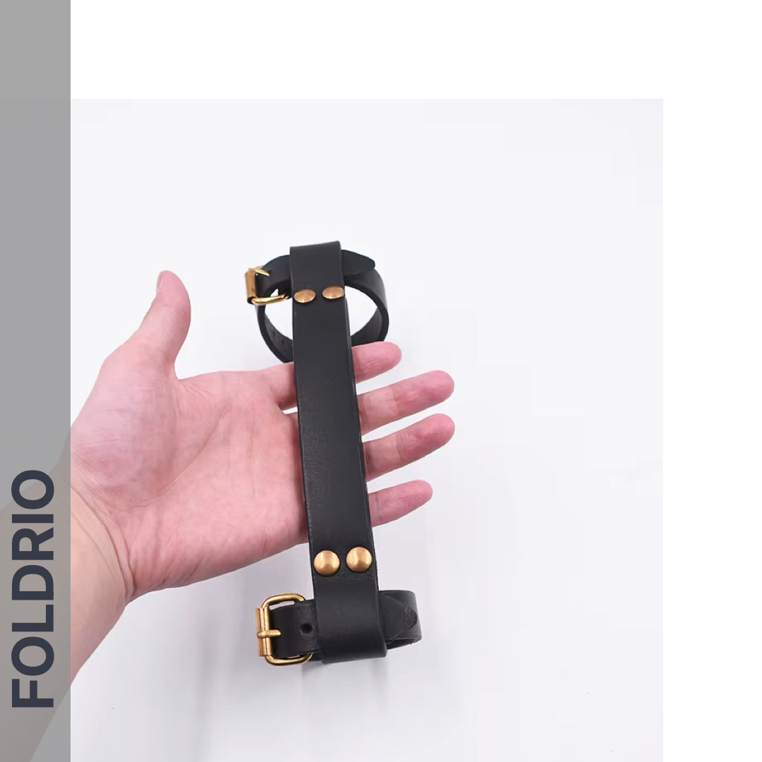 A hand holds the FOLDRIO Brompton Leather Carry Handle – Full-Grain with brass hardware, featuring adjustable buckle straps. The product is shown against a white background, with "FOLDRIO" displayed vertically on the left side of the image.