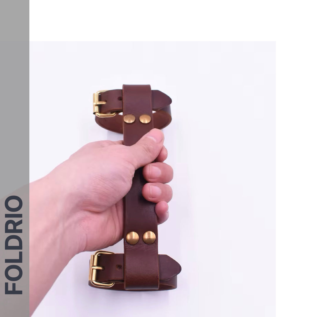 A hand holds the FOLDRIO Brompton Leather Carry Handle—full-grain leather with brass hardware—against a white background, with "FOLDRIO" displayed vertically on the left.