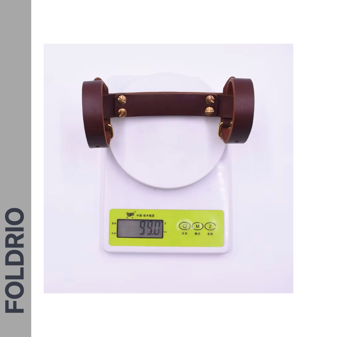 The Brompton Leather Carry Handle – Full-Grain, Brass Hardware by FOLDRIO rests on a digital scale reading 990g. The scale has a white base, green buttons, and "FOLDRIO" appears vertically on the left side.