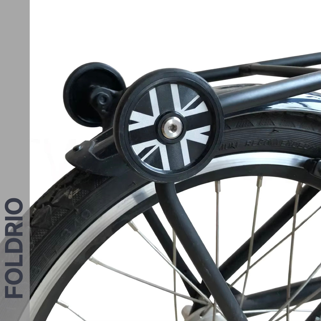A close-up shows a bicycle’s rear wheel fitted with FOLDRIO Brompton Easy Wheels Union Jack Edition with titanium bolts. "FOLDRIO" appears vertically on a grey strip to the left.