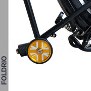 A close-up of the FOLDRIO Brompton Easy Wheels Union Jack Edition with Titanium Bolts, featuring a small yellow aluminum alloy wheel with a white Union Jack design on a black frame. The FOLDRIO logo appears vertically on a grey strip at the left edge.