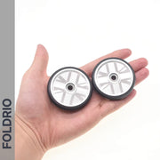 A hand holds two compact, silver and black Brompton Easy Wheels Union Jack Edition with titanium bolts by FOLDRIO; the brand name appears vertically on the left, accentuating these stylish aluminium bike wheels.