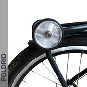 Close-up of Brompton Easy Wheels Union Jack Edition with titanium bolts by FOLDRIO. Aluminum alloy wheel and silver dynamo light above the tire. The word FOLDRIO appears vertically on a grey strip to the left.