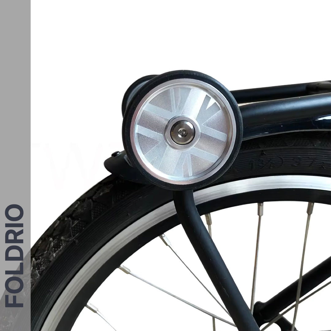 Close-up of Brompton Easy Wheels Union Jack Edition with titanium bolts by FOLDRIO. Aluminum alloy wheel and silver dynamo light above the tire. The word FOLDRIO appears vertically on a grey strip to the left.