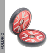 Two red FOLDRIO Brompton Easy Wheels Union Jack Edition with titanium bolts are shown—one upright, one flat—with black rubber edges. "FOLDRIO" appears vertically left. Perfect as replacement wheels for Brompton scooters.