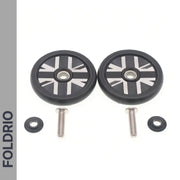 Two small black Brompton Easy Wheels Union Jack Edition with titanium bolts by FOLDRIO and two washers are displayed on a white background. A grey vertical strip on the left shows "FOLDRIO" in bold black letters.