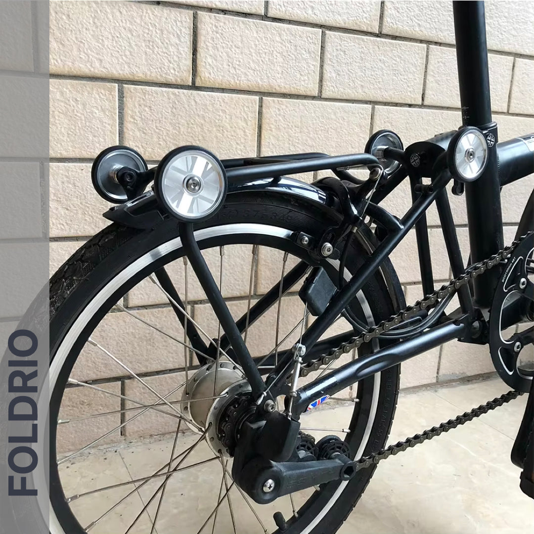 Close-up of a folding bike’s rear wheel and frame fitted with Brompton Easy Wheels Union Jack Edition with Titanium Bolts by FOLDRIO, "FOLDRIO" vertically on the left. Setup features durable AL7075 aluminum alloy components.