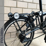 Close-up of a folding bike’s rear wheel and frame fitted with Brompton Easy Wheels Union Jack Edition with Titanium Bolts by FOLDRIO, "FOLDRIO" vertically on the left. Setup features durable AL7075 aluminum alloy components.