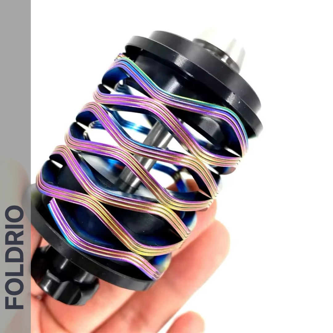 A hand holds a Brompton Rear Shock Absorber by FOLDRIO, a black cylindrical part wrapped with iridescent coiled wires; "FOLDRIO" appears vertically on the left side of the image.