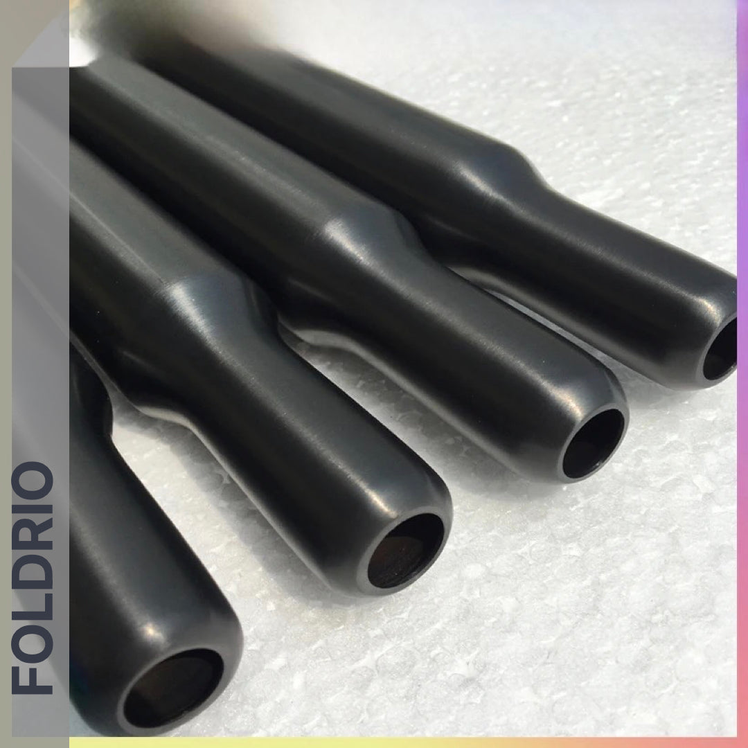 Four multicolour titanium cylindrical seatposts with rounded ends, branded FOLDRIO, are arranged parallel on a textured white surface. "FOLDRIO" is displayed vertically along the left side of the image.