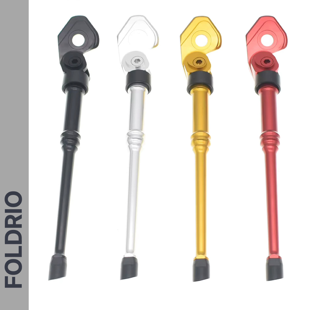 Four FOLDRIO Brompton Kickstand – Adjustable Aluminium, A and C Line models in black, silver, gold, and red with rear axle mounts stand vertically on a white background. "FOLDRIO" appears on a grey vertical strip to the left.