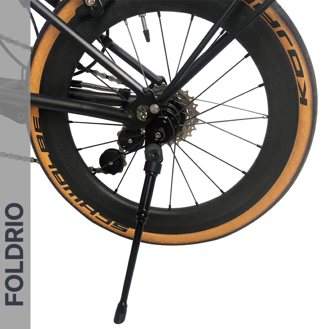Close-up of a bike's rear wheel with tan sidewall tire, visible gears, rear axle mount, and an extended Brompton Kickstand – Adjustable Aluminium (A & C Line) by FOLDRIO. The word FOLDRIO appears vertically on the left.