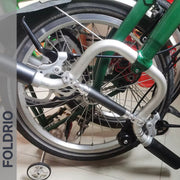A close-up shows the FOLDRIO Brompton M Handlebar Cross Brace – Adjustable, available in 6 colours, compactly arranged on a folded green bike. The word FOLDRIO appears vertically on the left side of the image.