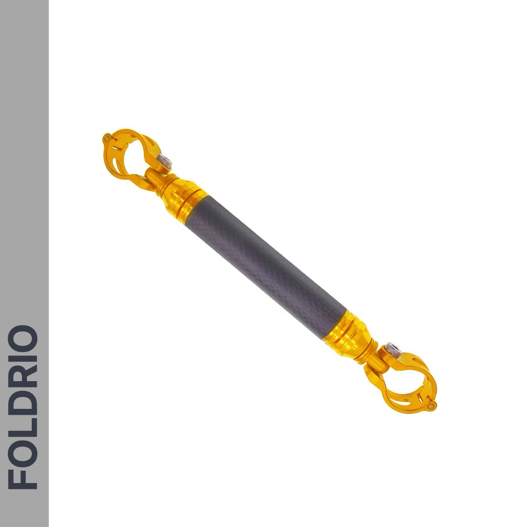 The FOLDRIO Brompton M Handlebar Cross Brace – Adjustable, 6 Colours, is a black and gold cylindrical rod with clamp mechanisms at both ends and a carbon fibre look. "FOLDRIO" appears vertically on a gray strip to the left.