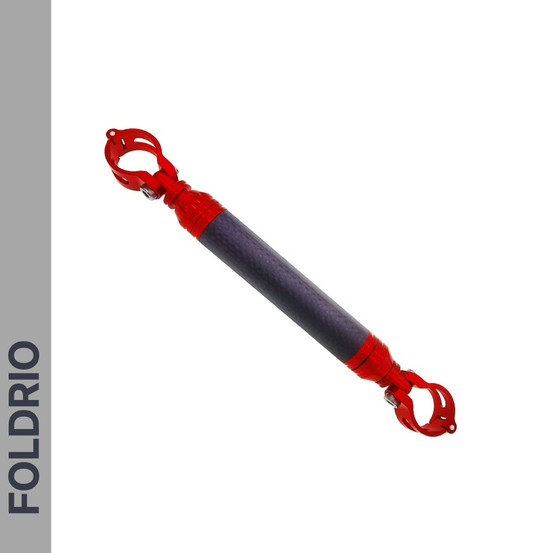 The Brompton M Handlebar Cross Brace – Adjustable by FOLDRIO is shown diagonally on a white background, featuring a textured dark center and red metal clamps. The word FOLDRIO appears vertically on a gray sidebar to the left.