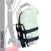 A Brompton Folding Bike frame features the FOLDRIO Brompton Front Bag Rack Holder with elastic straps securing a white roll-top dry bag. "FOLDRIO" appears vertically on the left against a mostly white background.