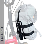 A light gray backpack is fastened to a red Brompton Folding Bike’s handlebars with FOLDRIO's Brompton Front Bag Rack Holder with Elastic Straps. The word "FOLDRIO" appears vertically on the left side of the image.
