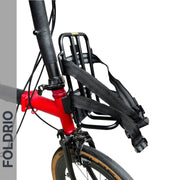 Close-up of the FOLDRIO Brompton Front Bag Rack Holder with elastic straps attached to a red foldable bike frame and handlebars. The brand name "FOLDRIO" appears vertically on the left side of the image.