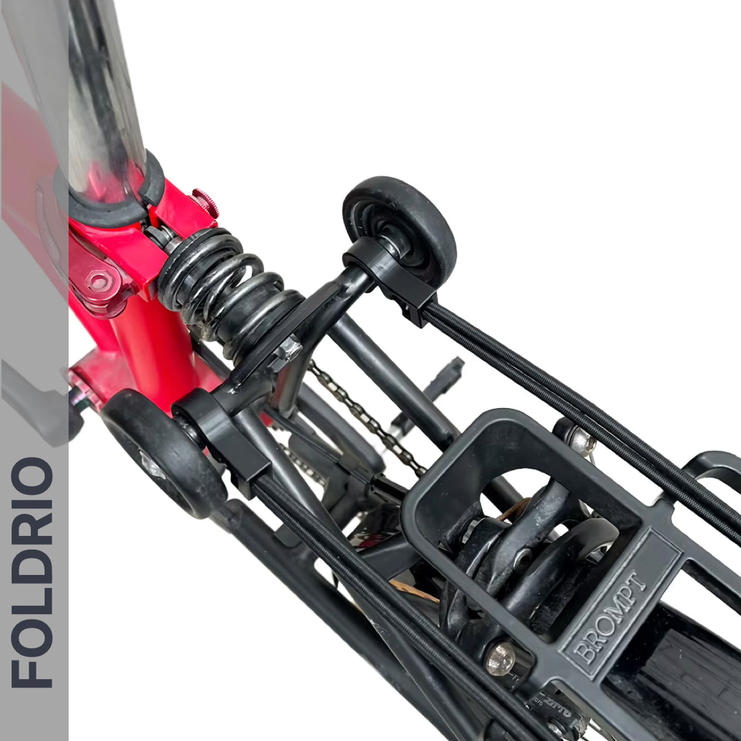 Top view of a folded red Brompton bike highlights the suspension, wheels, FOLDRIO Brompton Rear Rack Elastic Straps (fits AC Line & PT Line), and frame. "FOLDRIO" is shown vertically along the left side.