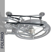 A folded bicycle is secured by Brompton Rear Rack Elastic Straps from FOLDRIO (fits AC Line & PT Line), with the word FOLDRIO displayed vertically on the left side. The wheels and frame are neatly aligned.