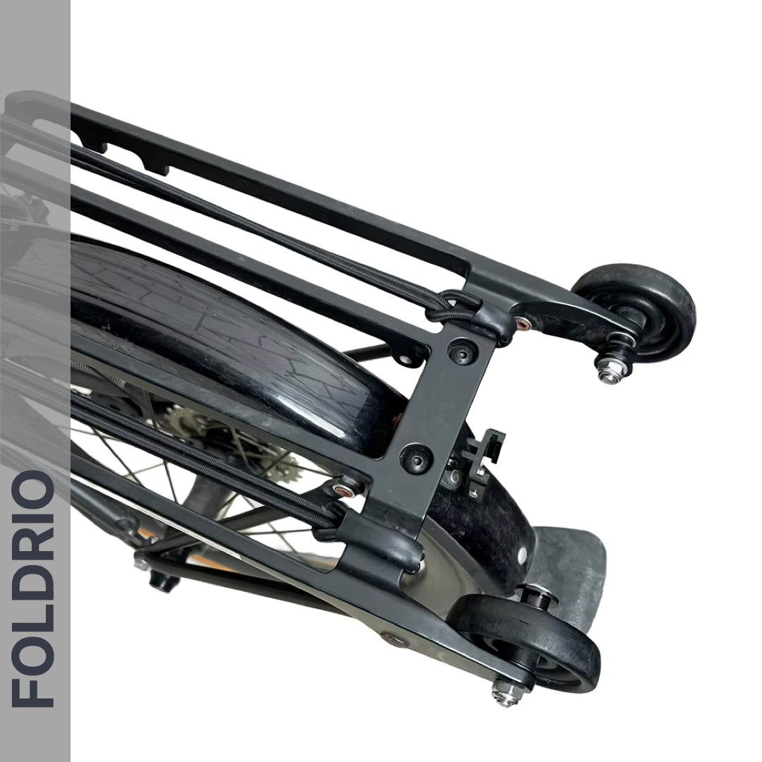 Close-up of a Brompton Rear Rack Elastic Strap by FOLDRIO (fits AC Line & PT Line), securing cargo on a bike with roller wheels for easy movement when folded. The word FOLDRIO appears vertically on the left side of the image.