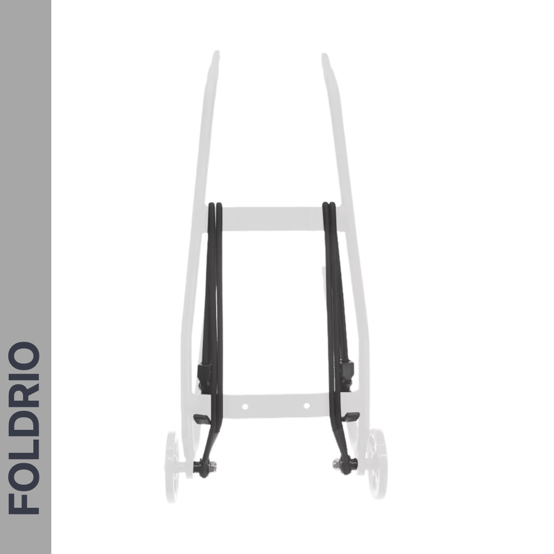 A partially visible wheeled cart shows the FOLDRIO brand vertically on the left; two black Brompton Rear Rack Elastic Straps, designed for AC Line (old) & PT Line (new), stand out on the light gray frame, resembling luggage straps.