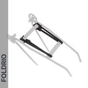 A FOLDRIO Brompton Rear Rack Elastic Strap secures a foldable metal stand with black hinges and wheels, shown with a transparent overlay to illustrate folding. The word FOLDRIO appears vertically on the left side. Fits AC Line (old) & PT Line (new).