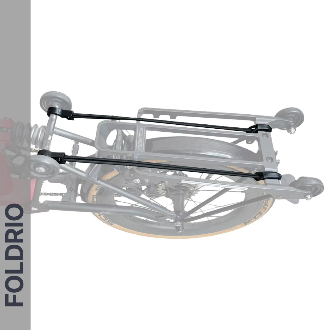 A grayscale close-up of a folded bicycle with a rear rack and FOLDRIO Brompton Rear Rack Elastic Straps – fits AC Line (old) & PT Line (new). "FOLDRIO" appears vertically on the left side against a gray background.
