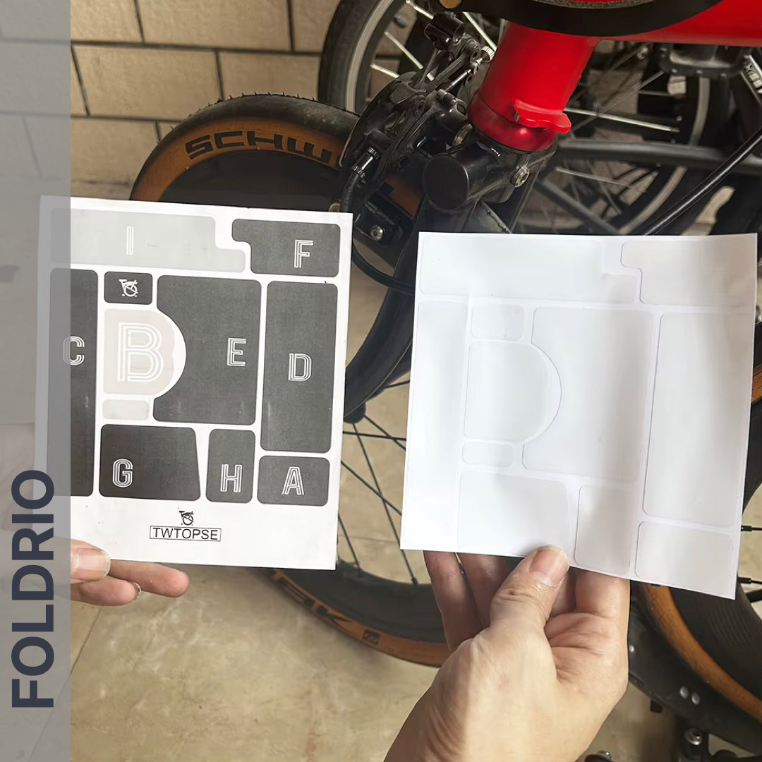 Brompton Brompton rear wheel shown as a hand holds two FOLDRIO Protective Sticker sheets, one labeled, beside the frame | Foldrio. Foldrio