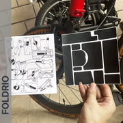 Brompton Brompton black FOLDRIO protective sticker set and instructions held before a red-framed bike; FOLDRIO branding shown | Foldrio. Foldrio