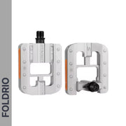 Two Brompton Foldable Flat Pedals – Lightweight Aluminium Upgrade, silver with black axles and reflective orange strips, featuring a rectangular open design, are shown on a white background. FOLDRIO appears vertically on the left. Ideal Brompton replacement.